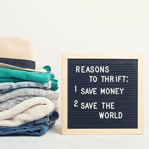 Stack of clothes next to a letter board with 'Reasons to Thrift' text on a white background